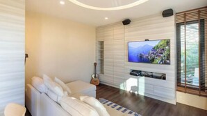 A modern living room with a flat-screen TV mounted on a wall, a white sofa, a guitar, and a wooden floor. - Jaidee Pool Villa (Hat Yai)