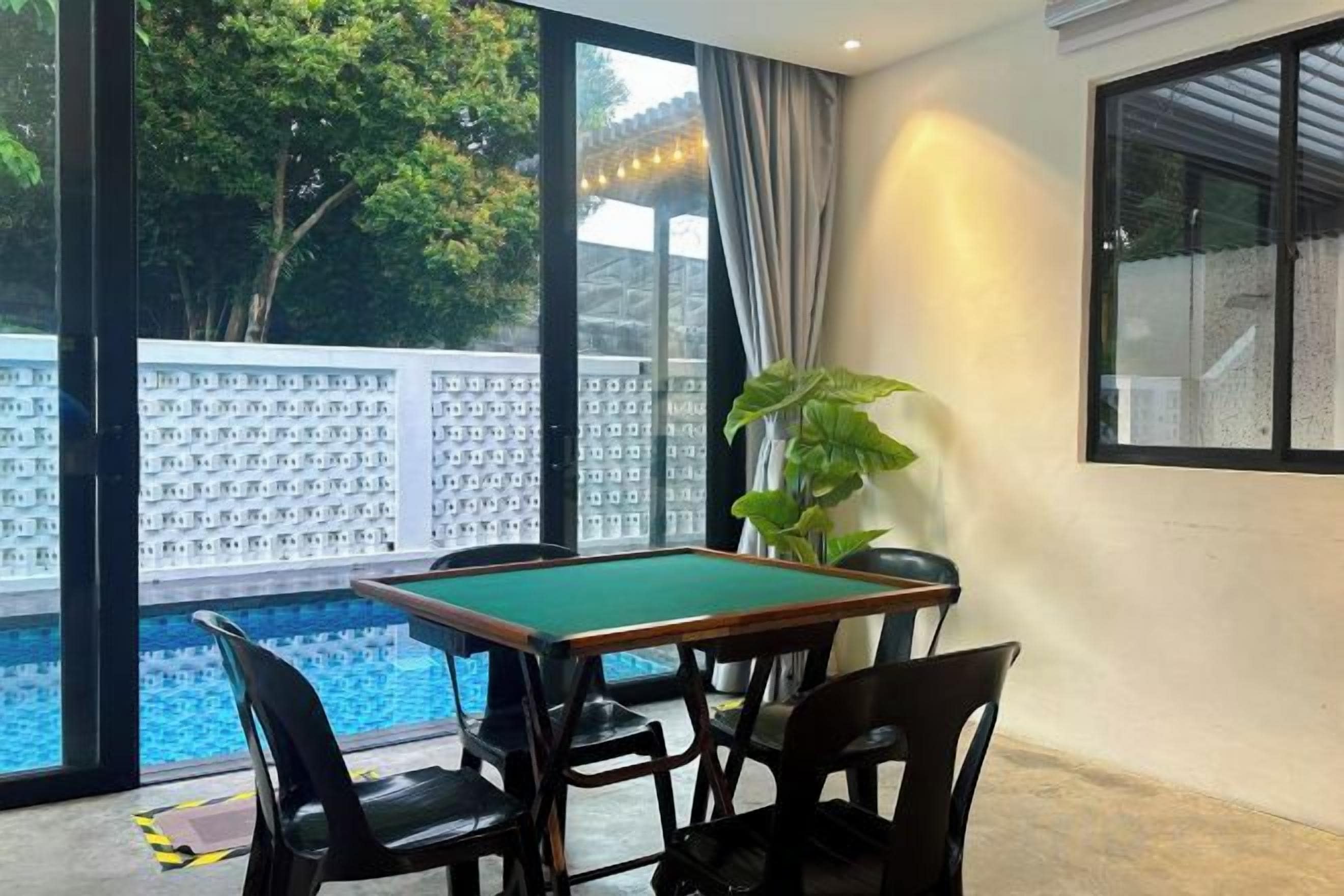Une table de billard avec quatre chaises, dans une pièce dotée de grandes fenêtres donnant sur une piscine.