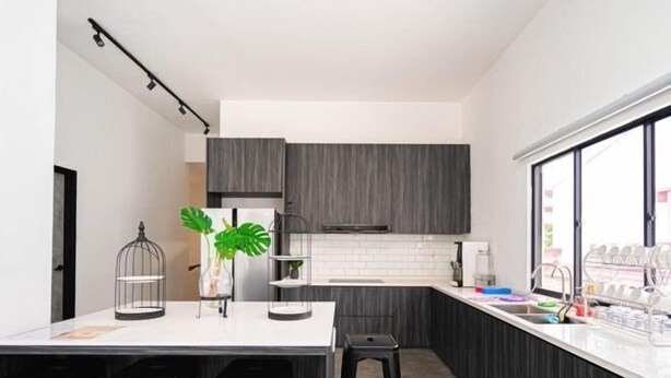 Une cuisine moderne avec des meubles de couleur sombre, un plan de travail blanc, un tabouret de bar et une fenêtre donnant sur un beau paysage.