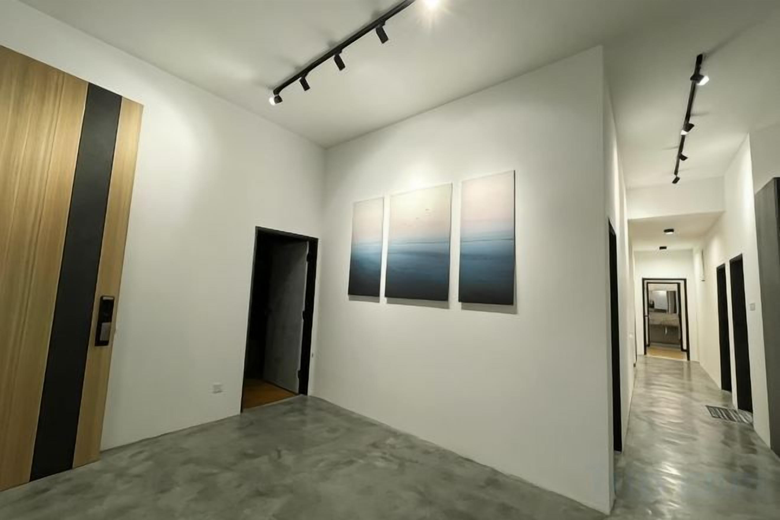 A hallway with a wooden door, a concrete floor, and three wall-mounted artworks.
