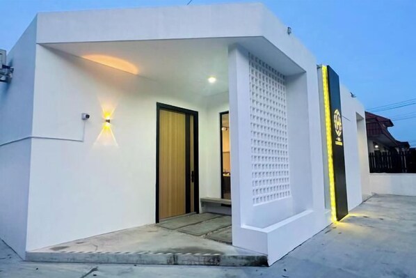 Un bâtiment moderne à l’extérieur blanc, doté d’une porte en bois et d’un petit hall d’entrée avec quelques marches.
