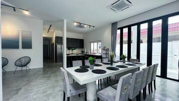 A modern dining area with a white table, grey chairs, and a kitchen in the background.