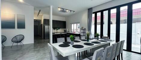 A modern dining area with a white table, grey chairs, and a kitchen in the background.