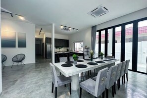 Un espace repas moderne avec une table blanche, des chaises grises et une cuisine en arrière-plan.