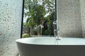 Une salle de bain moderne avec une baignoire sur pieds, une douche à parois de verre et une vue sur la verdure environnante.