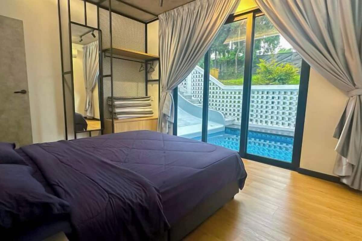 Ein Schlafzimmer mit Bett, einem Fenster mit Vorhängen, Blick auf einen Pool und einem Balkon.
