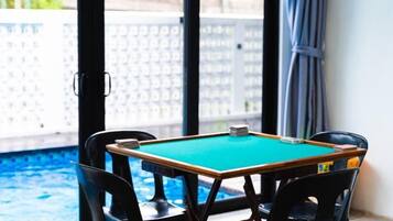 A pool table with four chairs, a pool, and a view of a white fence and trees.