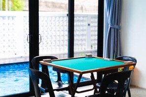 Een pooltafel met vier stoelen, een zwembad en uitzicht op een witte schutting en bomen.