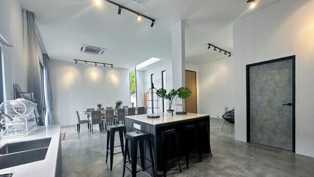 Een moderne keuken met een centraal eiland, barkrukken en een eethoek met stoelen en tafels.