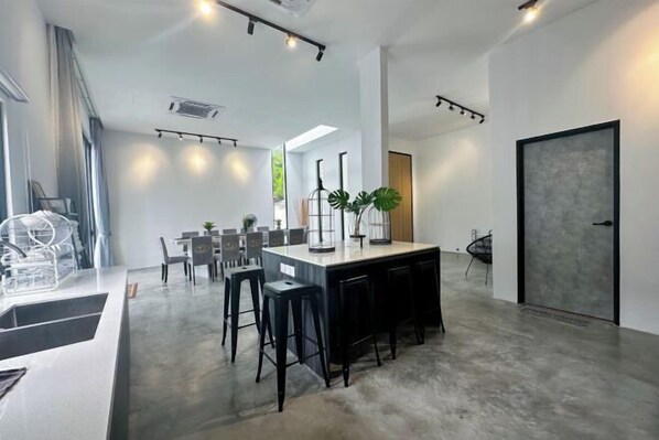 A modern kitchen with a central island, bar stools, and a dining area with chairs and tables. - The Luxurious 27, Johor Bahru (Johor Bahru)