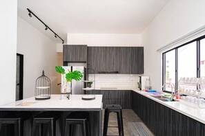 A modern kitchen with dark cabinets, a white countertop, and a bar stool. - The Luxurious 27, Johor Bahru (Johor Bahru)