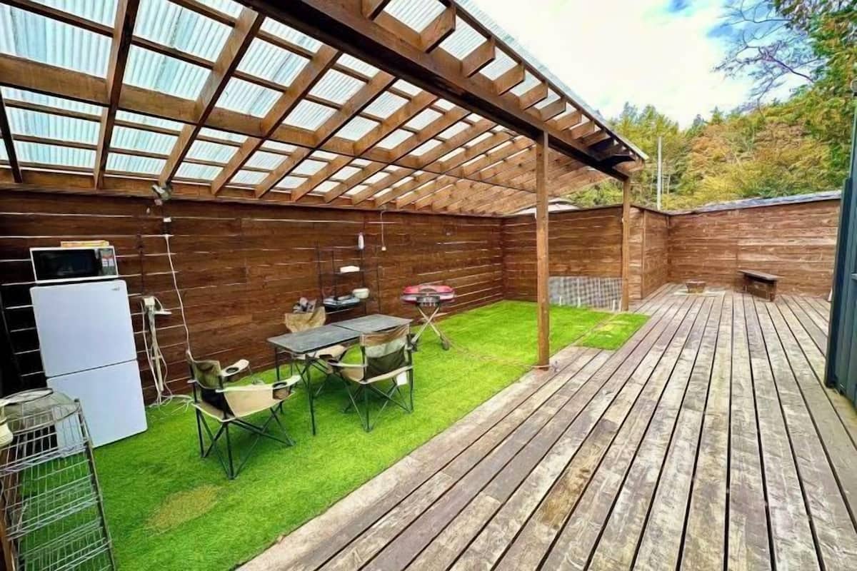 A wooden deck with a pergola, a barbecue grill, and a table with chairs.