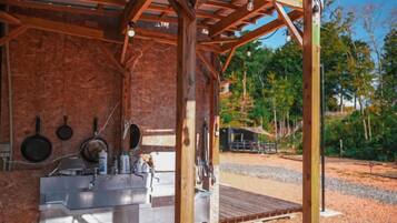 A rustic outdoor kitchen with a sink, hanging pans, and a wooden deck.