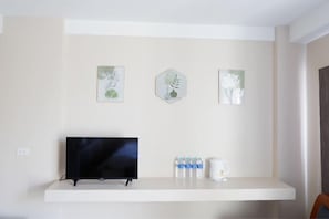 Ein Zimmer mit einem Flachbildfernseher auf einem weißen Regal, drei gerahmte botanische Drucke an der Wand und eine weiße Kaffeemaschine auf dem Regal.