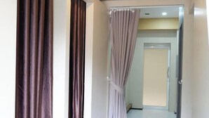 A hallway with a door at the end, a curtain partially drawn, and a tiled floor. - Shi-ro-i Poshtel (Hat Yai)