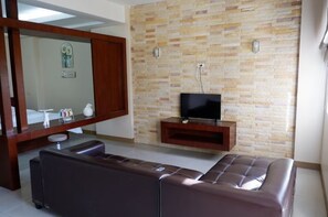 A modern living room with a stone-patterned wall, a large mirror, a flat-screen TV, and a leather sofa. - Shi-ro-i Poshtel (Hat Yai)
