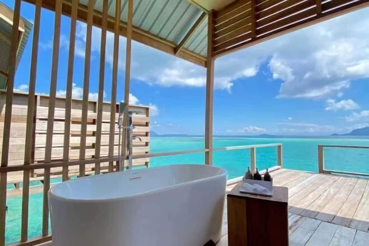 Een badkamer met een vrijstaand bad, houten dek en uitzicht op zee.