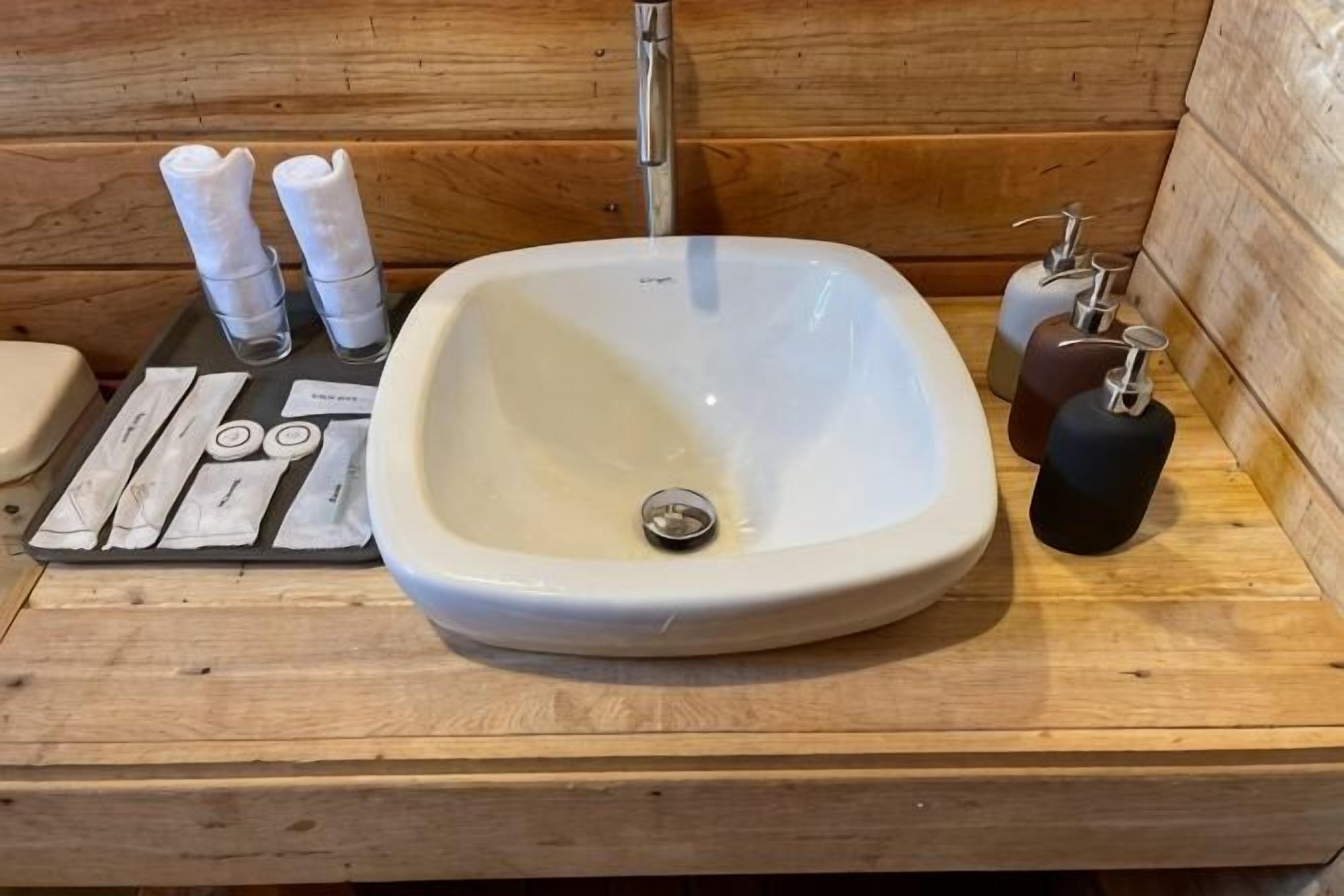 Une coiffeuse en bois avec un lavabo blanc, des distributeurs de savon et un ensemble de rasoirs.