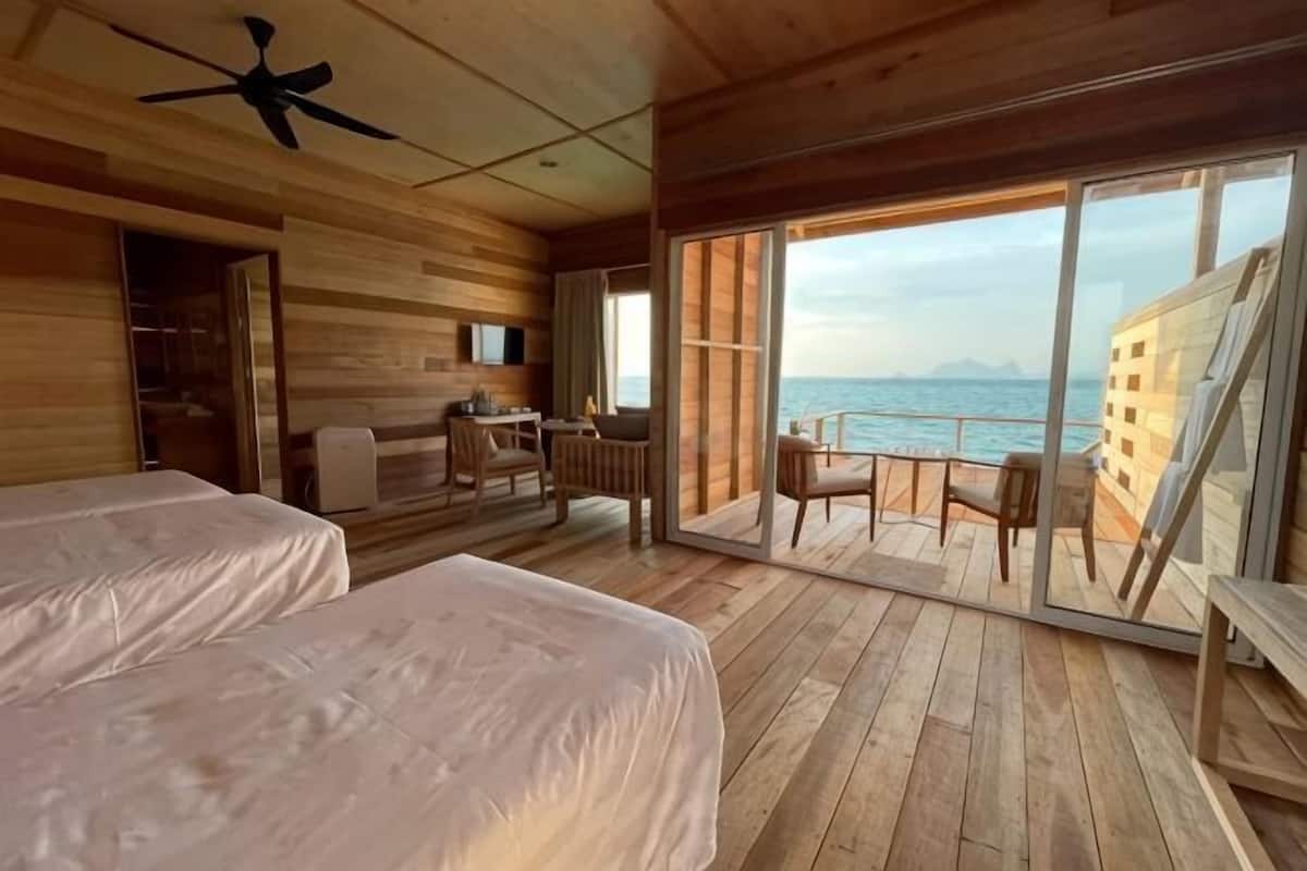 Een houten hut met twee bedden, een bureau en een balkon met uitzicht op zee.