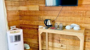 Interior de una cabaña de madera con una mesa de madera, una tetera, tazas y un televisor montado en la pared.
