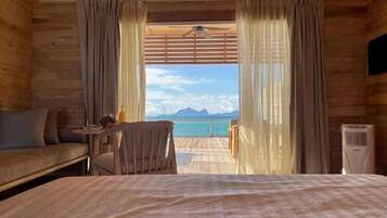 Una habitación de madera con una cama, una silla, una mesita con una botella y vistas al mar.
