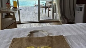 A hotel room with a bed, a table with a bottle and snacks, a chair, and a view of the ocean. - Sisipan Island Water Resort (Semporna)