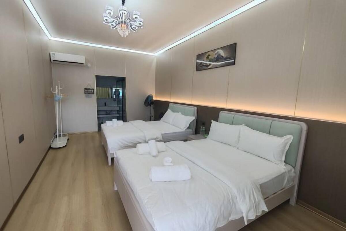 A hotel room with two beds, a chandelier, a painting on the wall, and a bedside table.