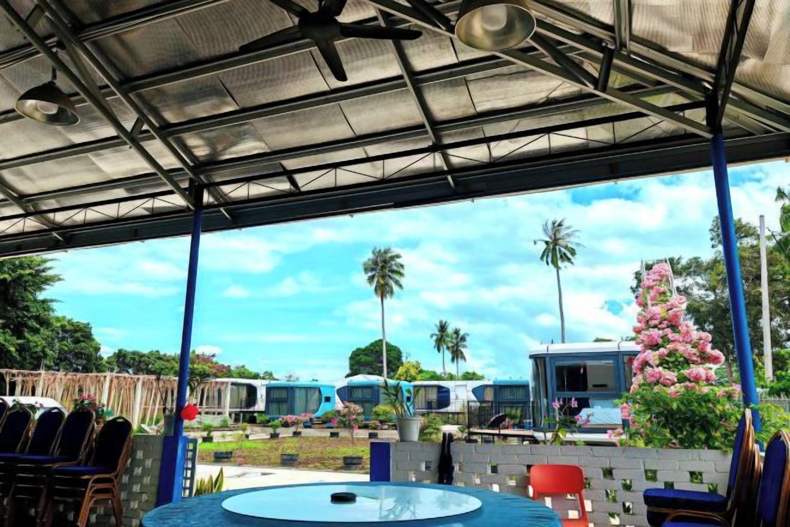 An outdoor covered area with a pool table, seating, and a view of parked buses and palm trees.