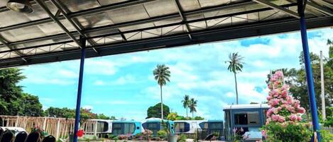 An outdoor covered area with a pool table, seating, and a view of parked buses and palm trees.