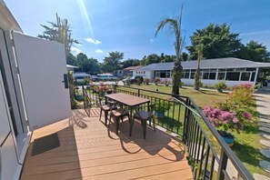 A balcony with a table and chairs, a view of a garden, and a building in the background. - Seawind Garden (Semporna)