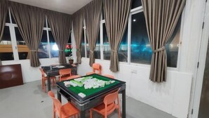 A room with a green felt table for playing mahjong, orange chairs, and large windows with curtains. - Seawind Garden (Semporna)