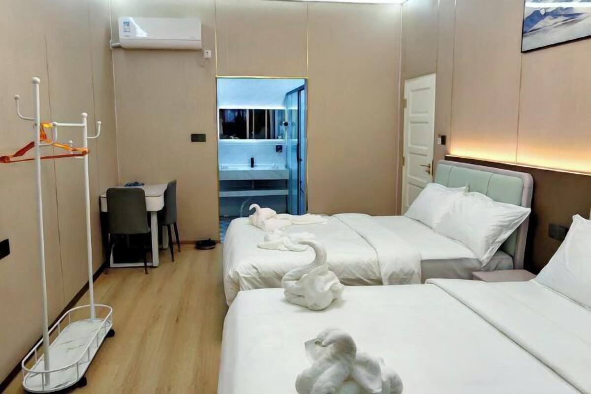 A hotel room with two beds, a desk, and a bathroom visible through an open door.