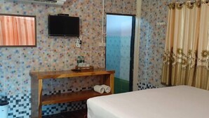 A hotel room with a bed, a wooden bedside table with a bottle and a tissue box, a TV mounted on the wall, and a bathroom door.
