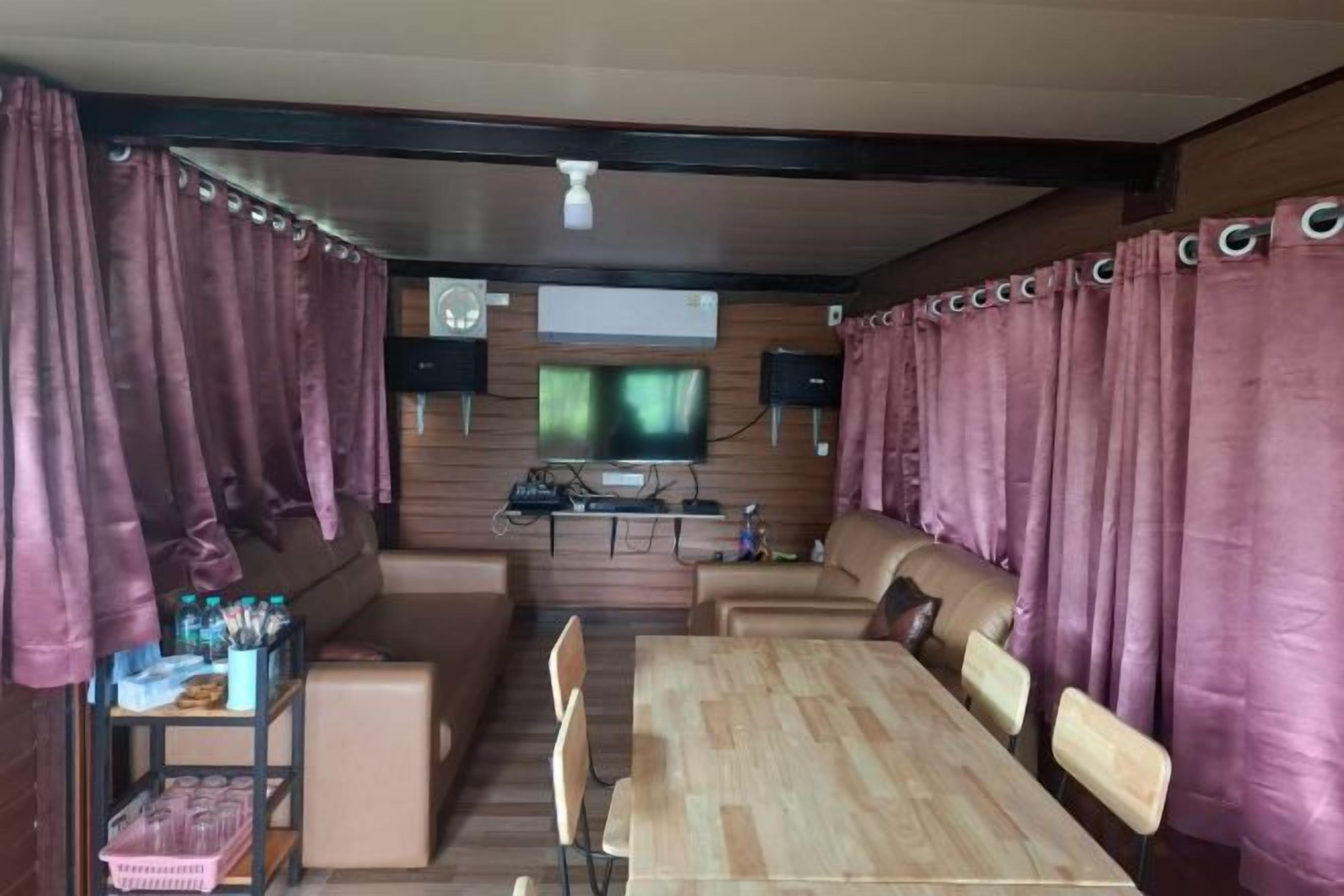 A room with a wooden dining table, cushioned seating, a television, and curtains.