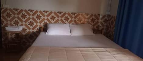 Habitación de hotel con cama, almohadas, mesita de noche y una toalla doblada, y pared con diseño.