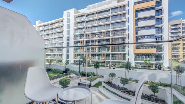 En modern lägenhetsbyggnad med flera balkonger, utomhusområden med sittplatser och en välskött trädgård.