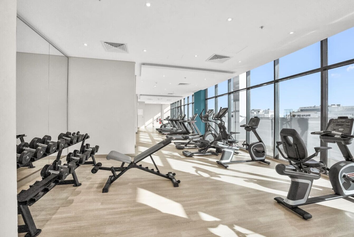 A modern gym with various exercise equipment, large windows, and a clean, bright interior.