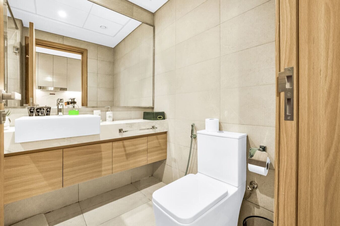 Un baño moderno con inodoro blanco, lavabo con espejo y zona de ducha.