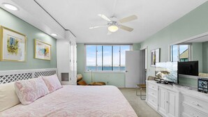 A bedroom with a bed, a TV, a dresser, and a window with a view of the sea.
