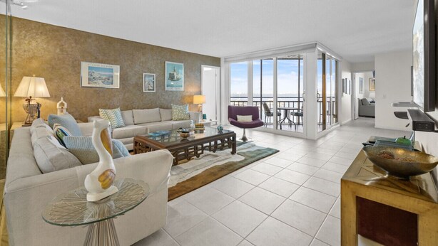 A spacious living room with a sofa, coffee table, and decorative items. There is a balcony with a view.