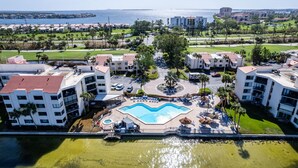 A resort with a central swimming pool, multiple buildings, and a view of the ocean.