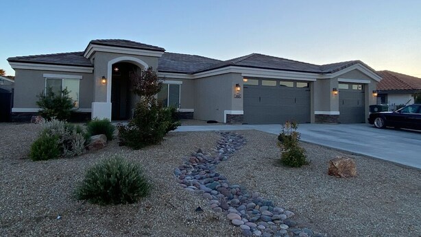 A modern two-story house with a garage, a driveway, and a landscaped front yard with rocks and shrubs.