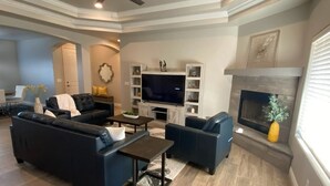 A spacious living room with a large TV, comfortable seating, and a fireplace.