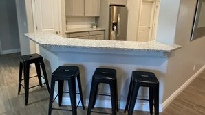 A kitchen with a granite countertop, white cabinets, a stainless steel refrigerator, and three black bar stools.