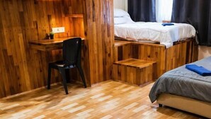 Ein Zimmer mit einem Holztisch, einem Stuhl, einem Bett mit grauer Decke und Holzboden.