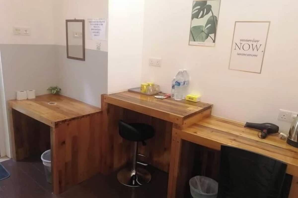 A small kitchenette with a wooden countertop, a black stool, and a trash bin.