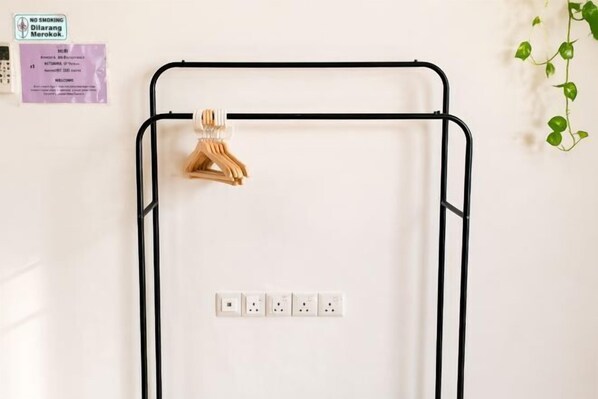 Un tendedero metálico con perchas de madera, un enchufe eléctrico fijado a la pared y un cartel de 'NO FUMAR'.