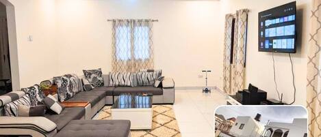 A modern living room with a sectional sofa, a coffee table, and a flat-screen TV mounted on the wall.