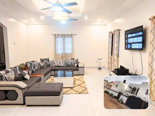 A modern living room with a sectional sofa, a coffee table, and a flat-screen TV mounted on the wall.