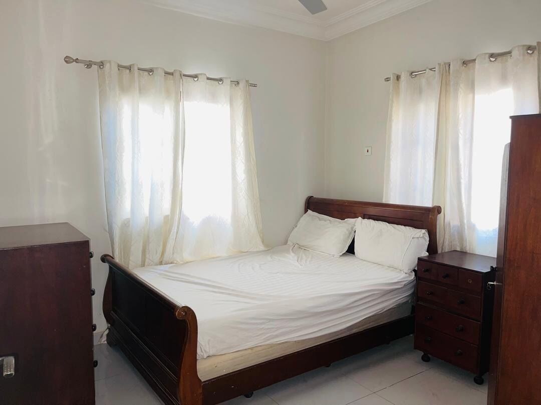 A bedroom with a wooden bed, white curtains, and a wooden dresser.